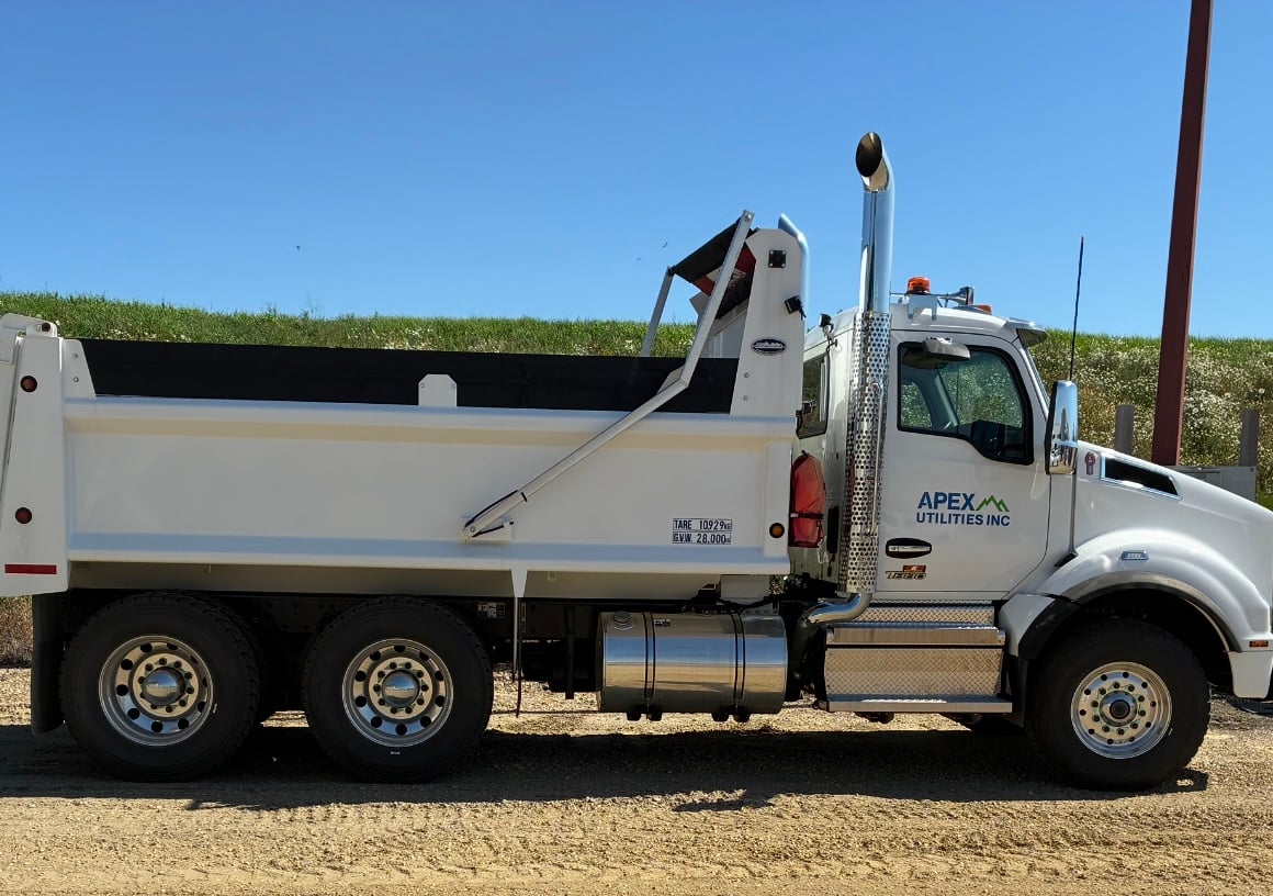White Apex Utilities dump truck parked on gravel under a clear blue sky