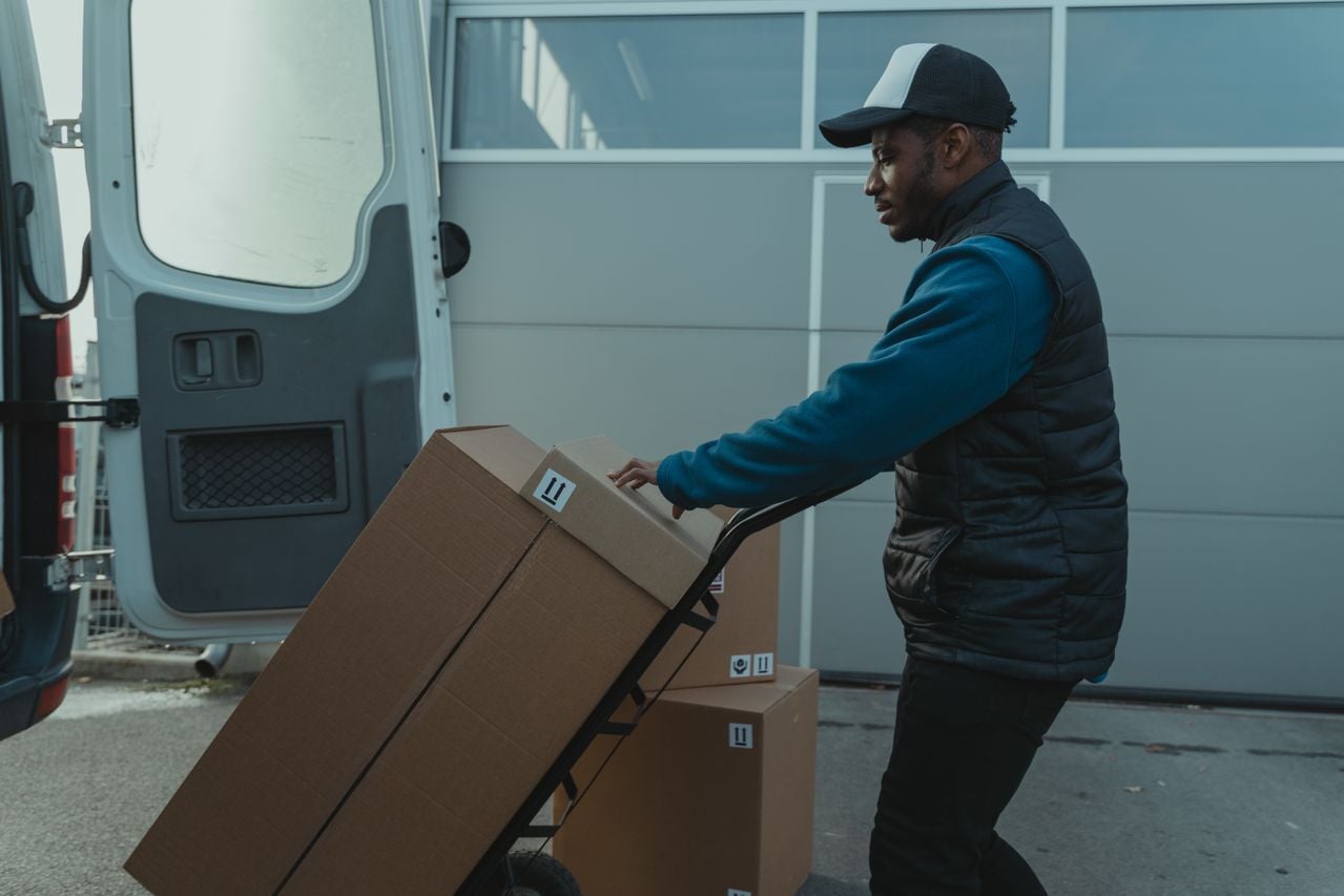 A driver delivers cardboard boxes using a dolly outdoors during high volume holiday season