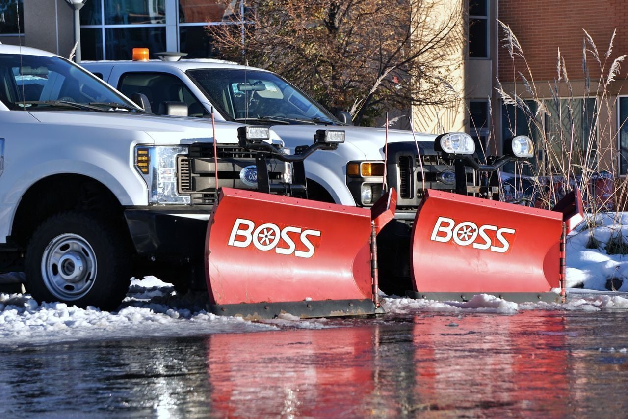 Two white fleet pickup trucks equipped with red Boss snow plows parked in a snowy lot.